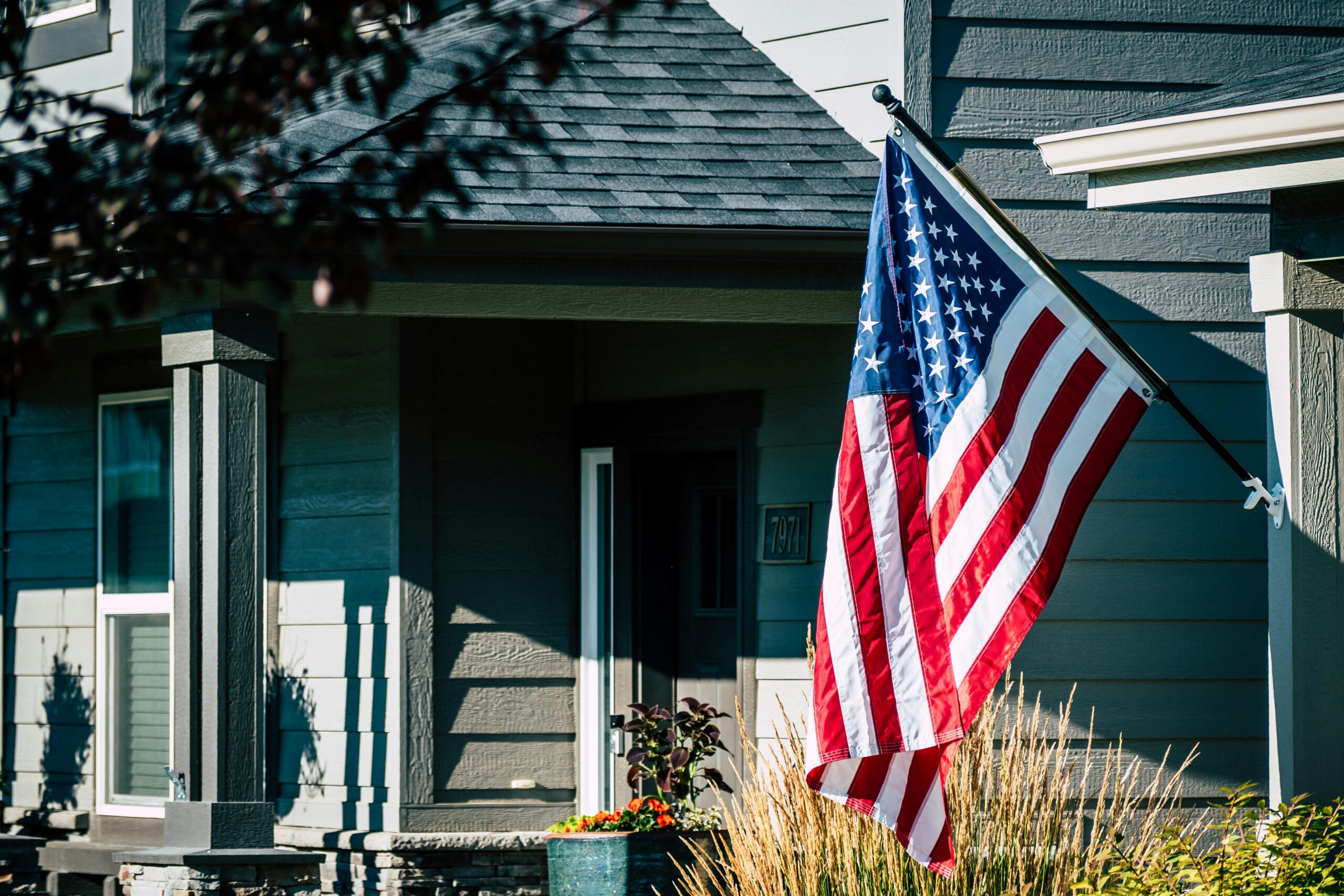 Big national US flag hanging outside contemporary wooden house on sunny summer weather